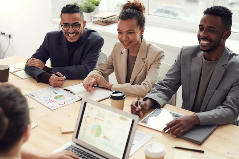A team reviewing sales charts on a laptop and printed reports around a meeting table